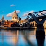 St Paul's Cathedral in London, England on a sunny day with the millennium bridge in the foreground spanning the River Thames.