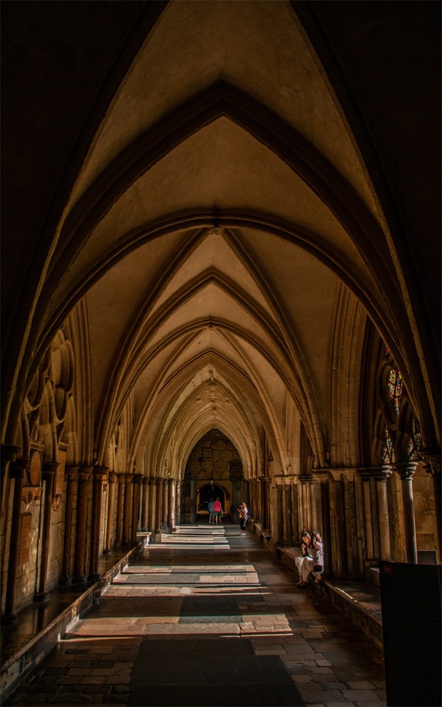 A cloister at Westminster Abbey showing the elaborate gothic architecture and the ribbed vaulted ceiling.